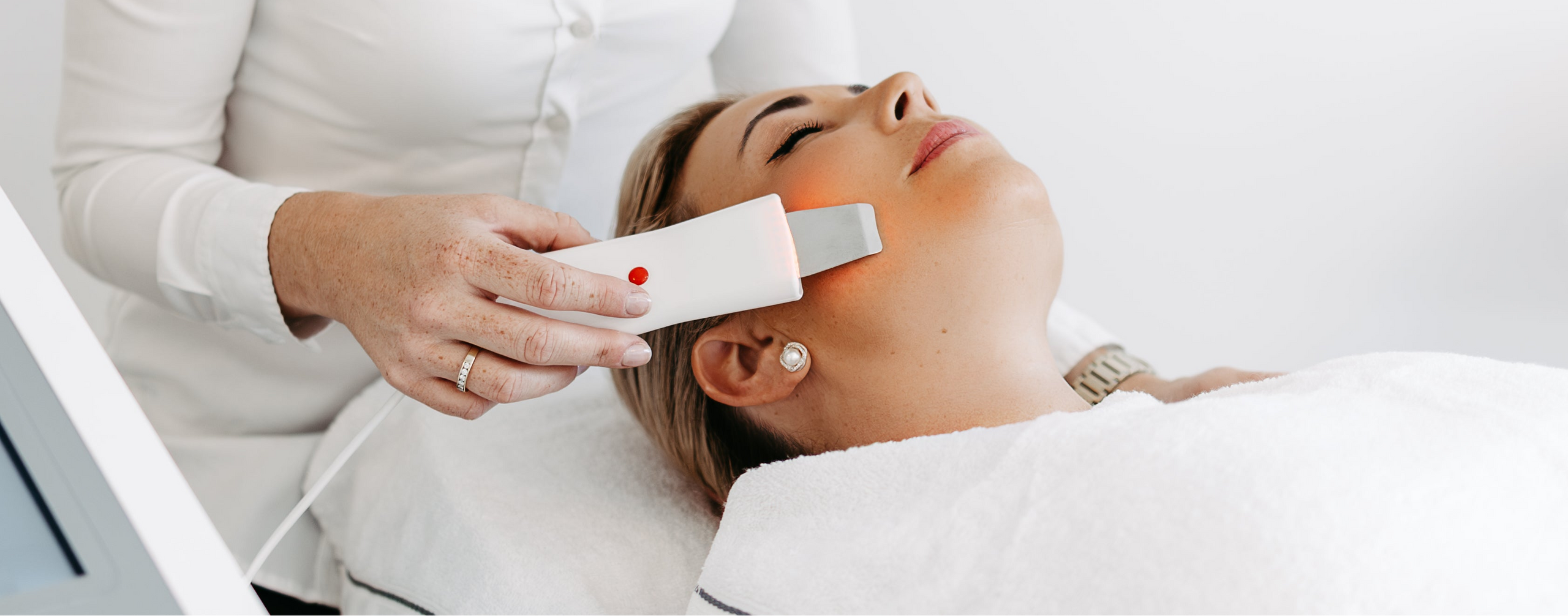 Woman receiving a facial treatment with a device from a professional in a clinical setting.
